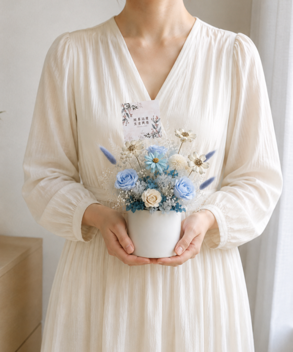 台灣女生雙手捧著藍色系永生花盆花，搭配淺藍玫瑰、白色花材與賀卡，奶油色自然光居家情境，適合生日、開幕與祝賀送禮