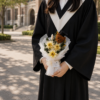 穿著學士袍的畢業生在大學校園手拿奶油色畢業花束，搭配小熊學士帽裝飾
